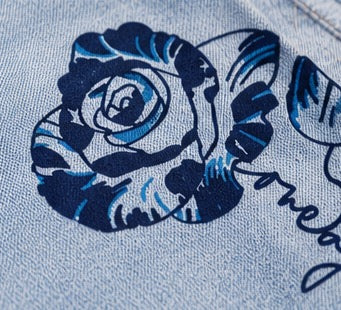 Nahaufnahme der Rosen-Stickerei mit dem Markenschriftzug auf dem Stoff.